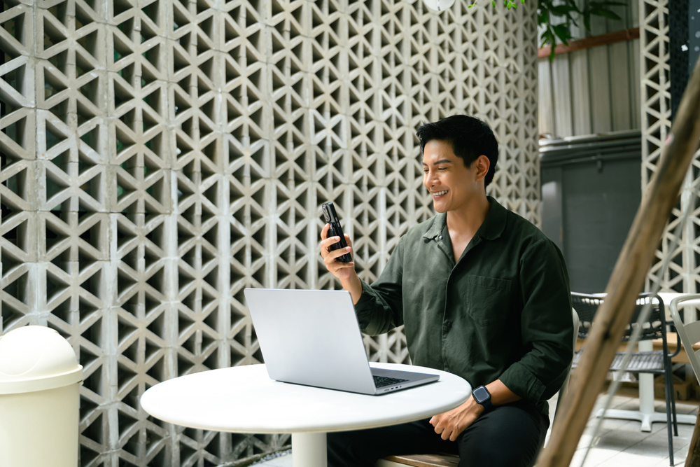 Smiling man having video call while working remotely on laptop at an outdoor urban cafe