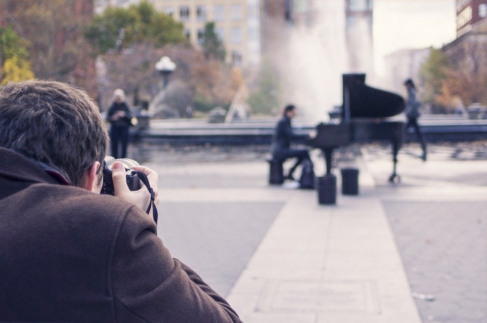 A street photographer photographing a pianist on the street playing the piano