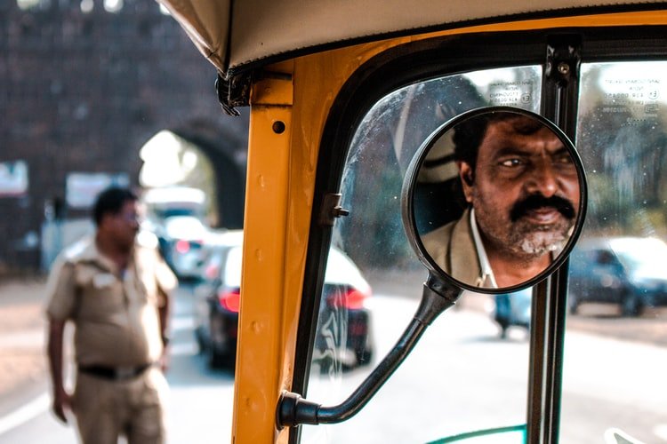 the face of a person reflecting in a mirror of an auto rickshaw