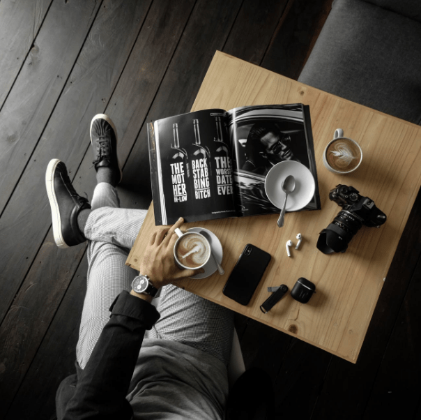 top-view-of-a-table-with-man-holding-a-cup-of-latte-with-a-magazine-camera-cellphone-and-other-personal-effects